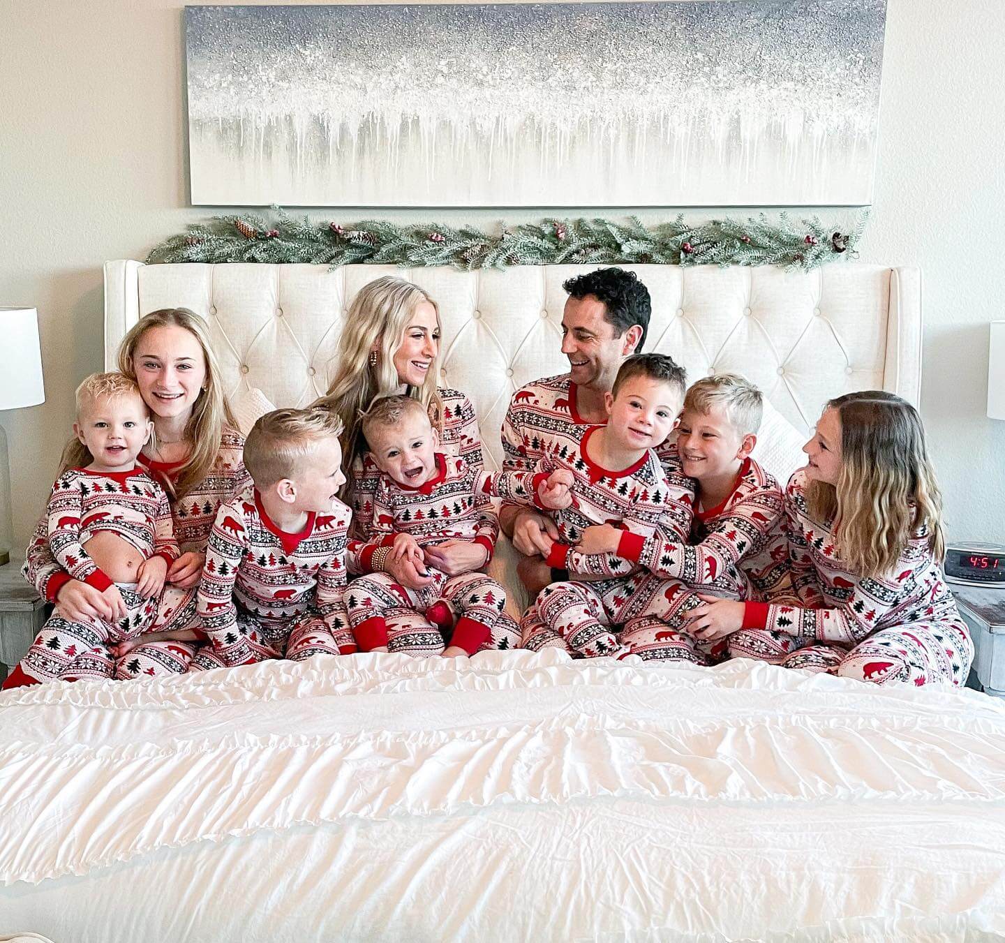 Family wearing matching Christmas pajamas with dog in front of a decorated Christmas tree
