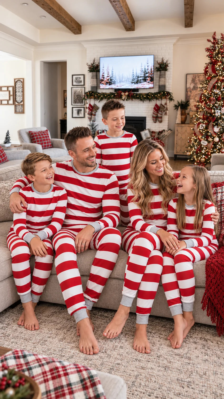 Family in red and white striped Christmas pajamas sitting on a sofa with a tree and white brick fireplace behind.