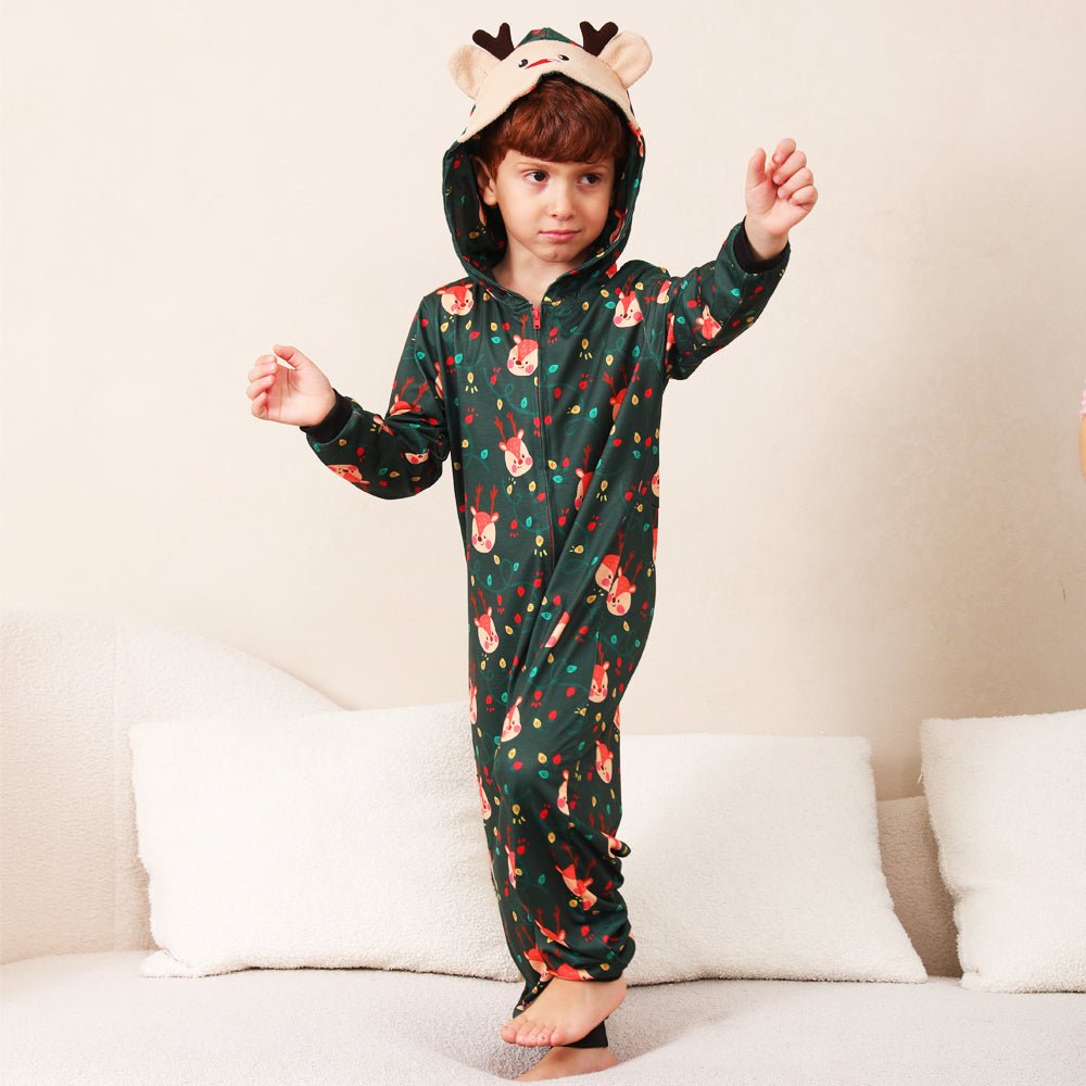 Young boy standing on a sofa in a green Christmas print onesie with a reindeer face hood and antlers.