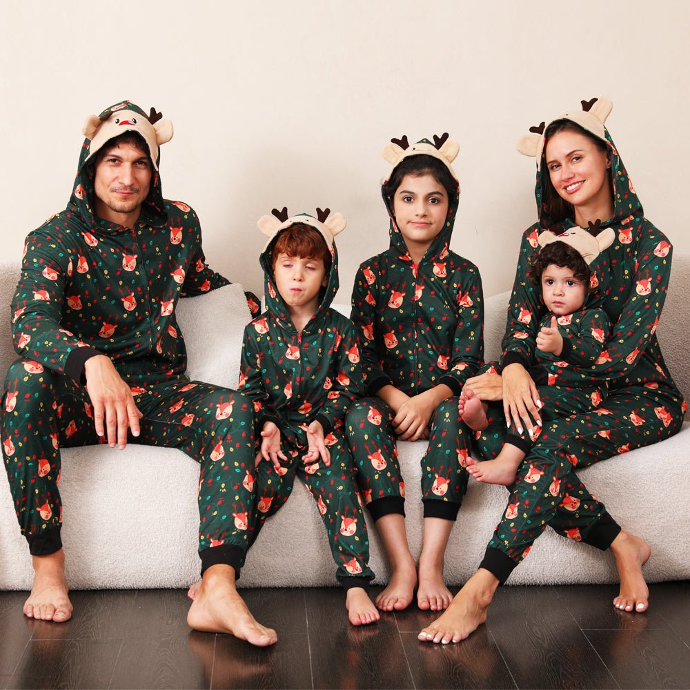 Parents and three children sitting on a sofa in green Christmas print onesies with reindeer face hoods and antlers.
