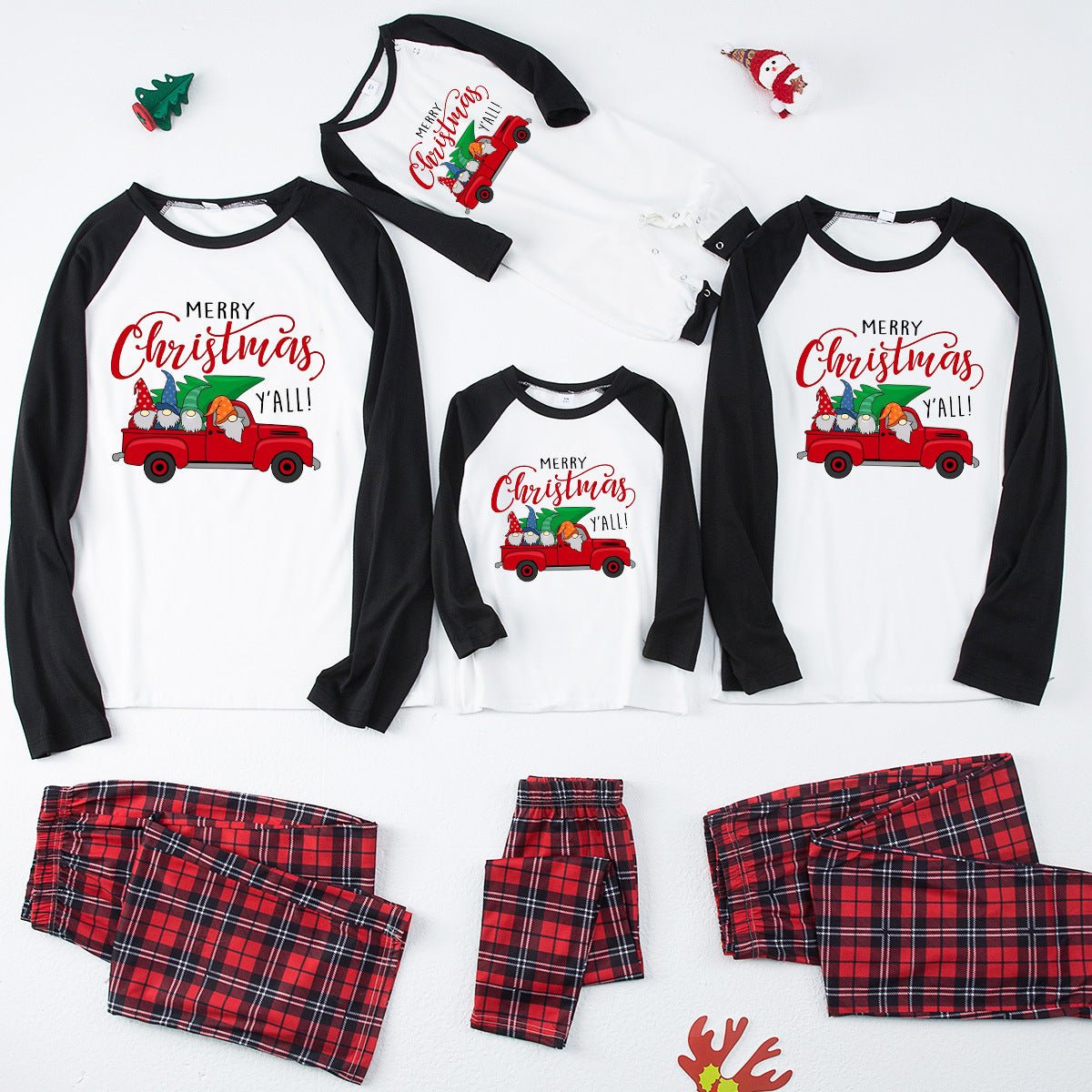 Pigiami natalizi per la famiglia con maglie con camion rosso, maniche nere, pantaloni in tartan rosso e tutina per neonato, disposti in piano.