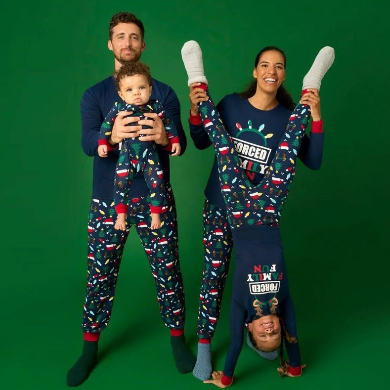 Parents holding a baby and an upside-down child in navy Forced Family Fun Christmas pajamas against a green backdrop.