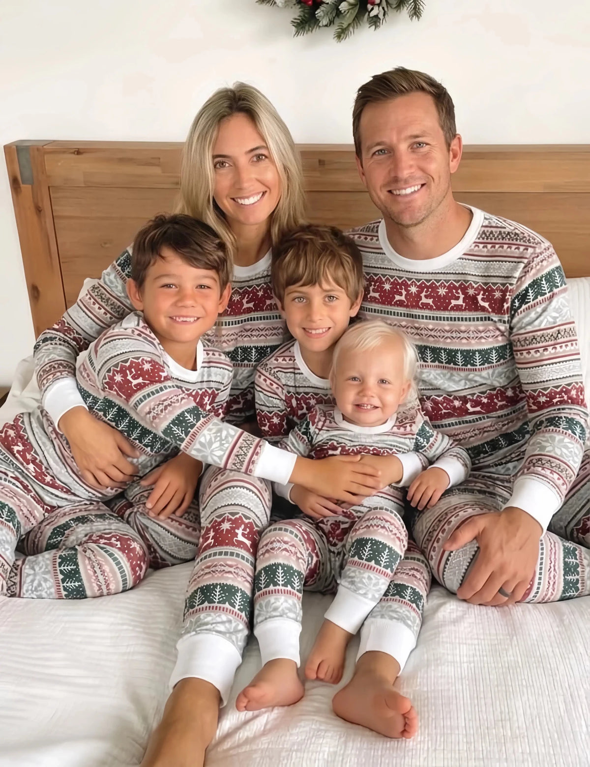 Parents and three children cuddling on a bed in red, green and white Fair Isle Christmas pajamas with white cuffs.