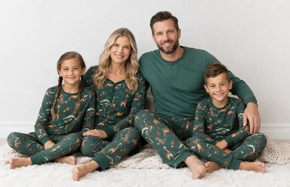 Famiglia seduta su un tappeto bianco in pigiami verdi con animali; il padre indossa una maglia Henley verde in tinta unita.