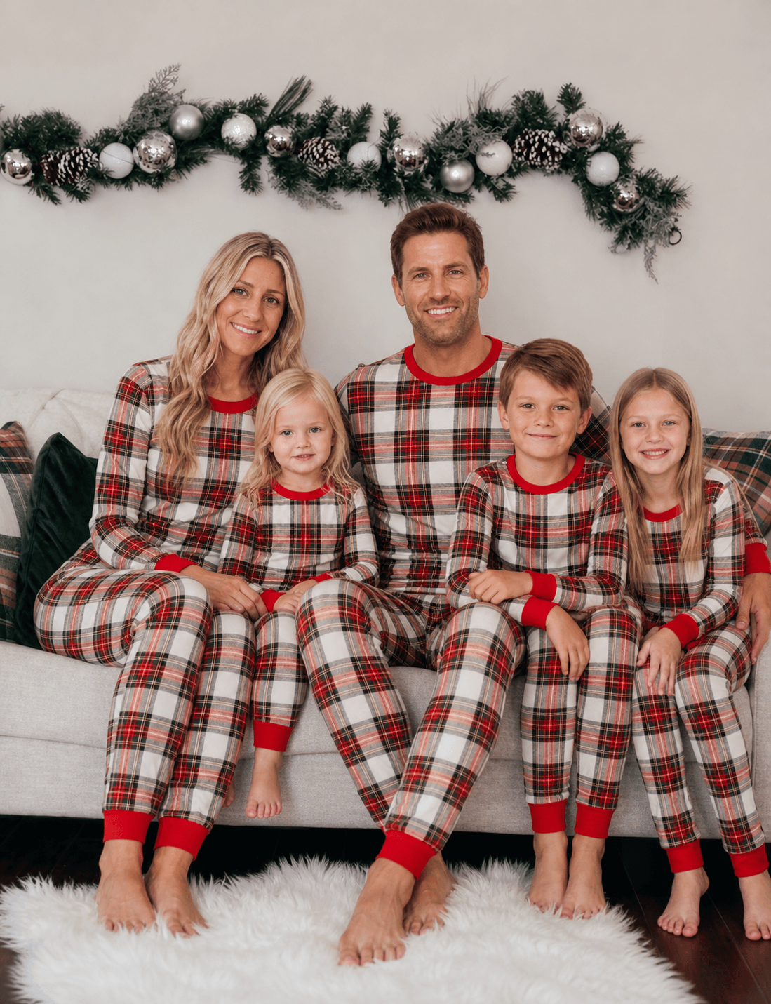 Parents and three children on a sofa in beige, red and black tartan Christmas pajamas with red cuffs.