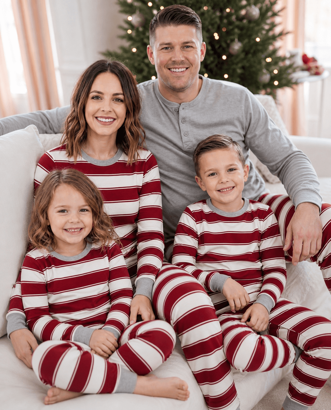 Famiglia comodamente seduta insieme su un divano bianco, in abbigliamento da notte festivo coordinato a righe rosse e bianche