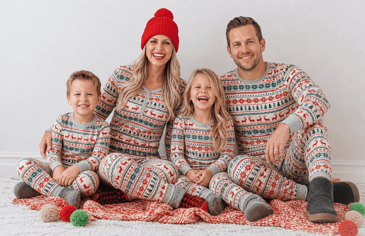 Famiglia seduta su una coperta rossa lavorata a maglia, in pigiami natalizi Fair Isle coordinati rossi e verdi, su sfondo bianco.