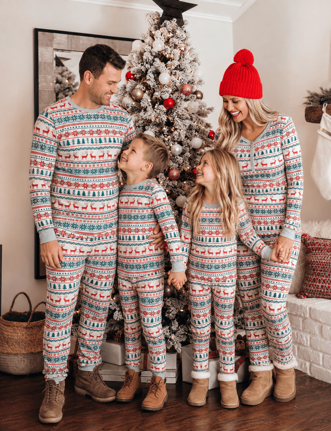 Parents and children looking at each other beside a Christmas tree in matching reindeer and tree print pajamas.