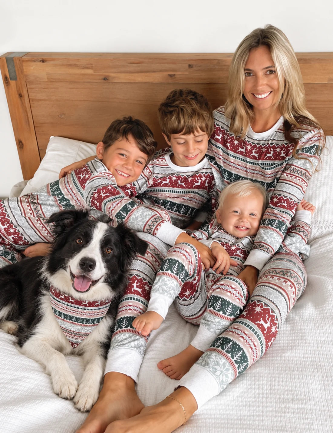 Family in red and white Fair Isle Christmas pajamas on a bed, with a dog wearing a matching bandana.