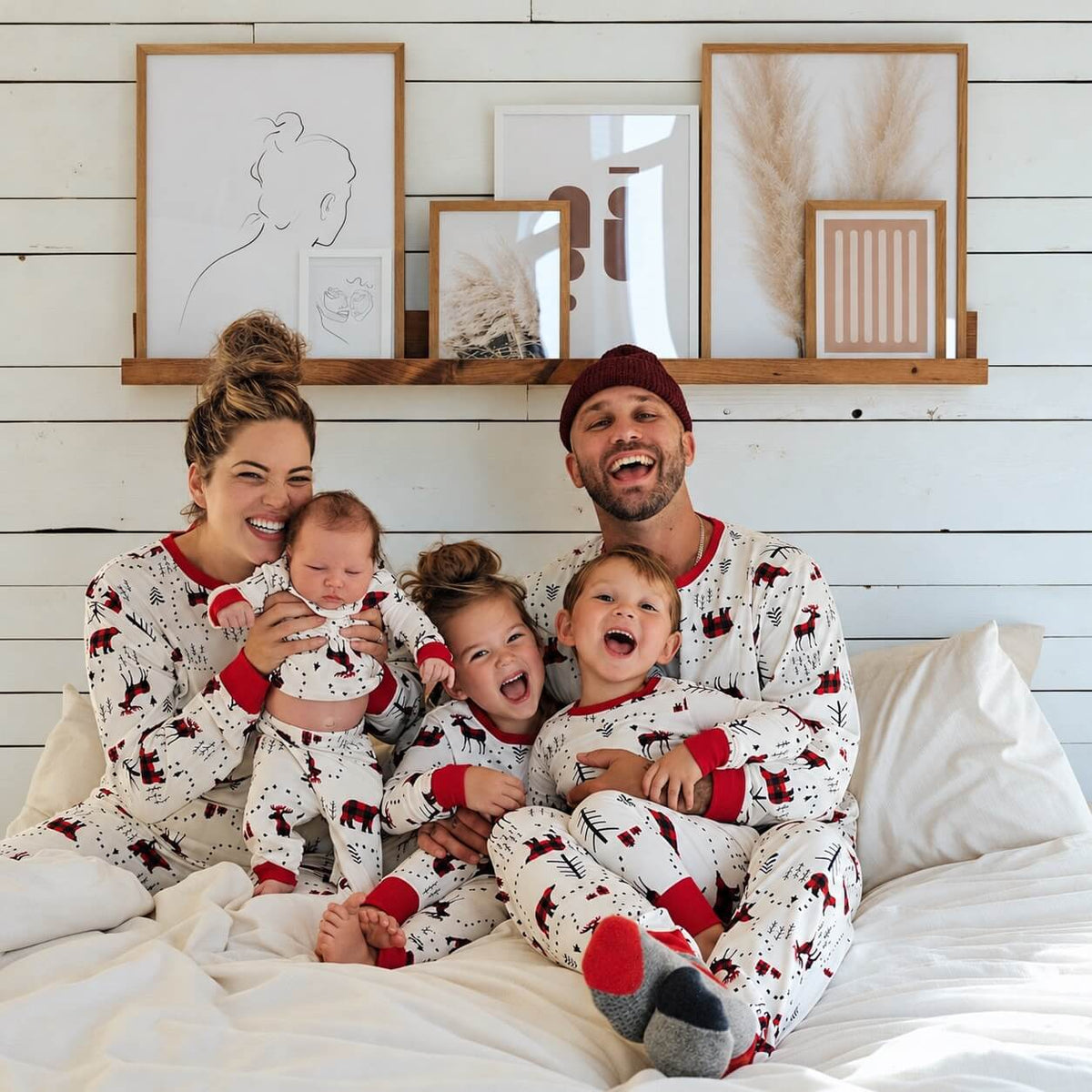 Parents and three children wearing matching white woodland-print pajamas while seated on a white bed.