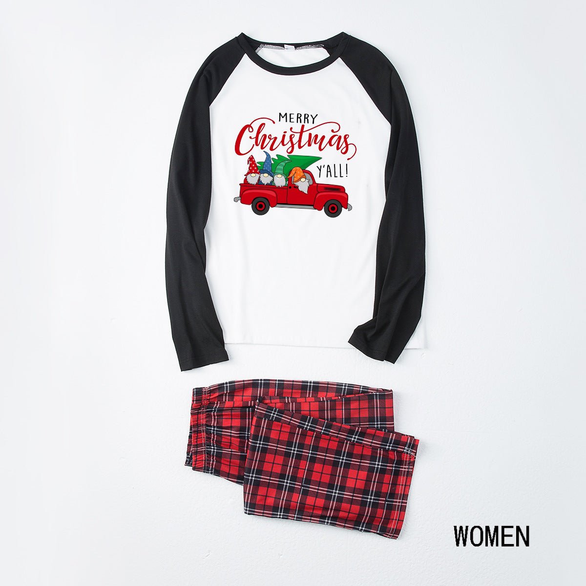 Pigiama da donna disposto in piano, con maglia bianca Merry Christmas Y'all con camion, maniche raglan nere e pantaloni in tartan rosso.