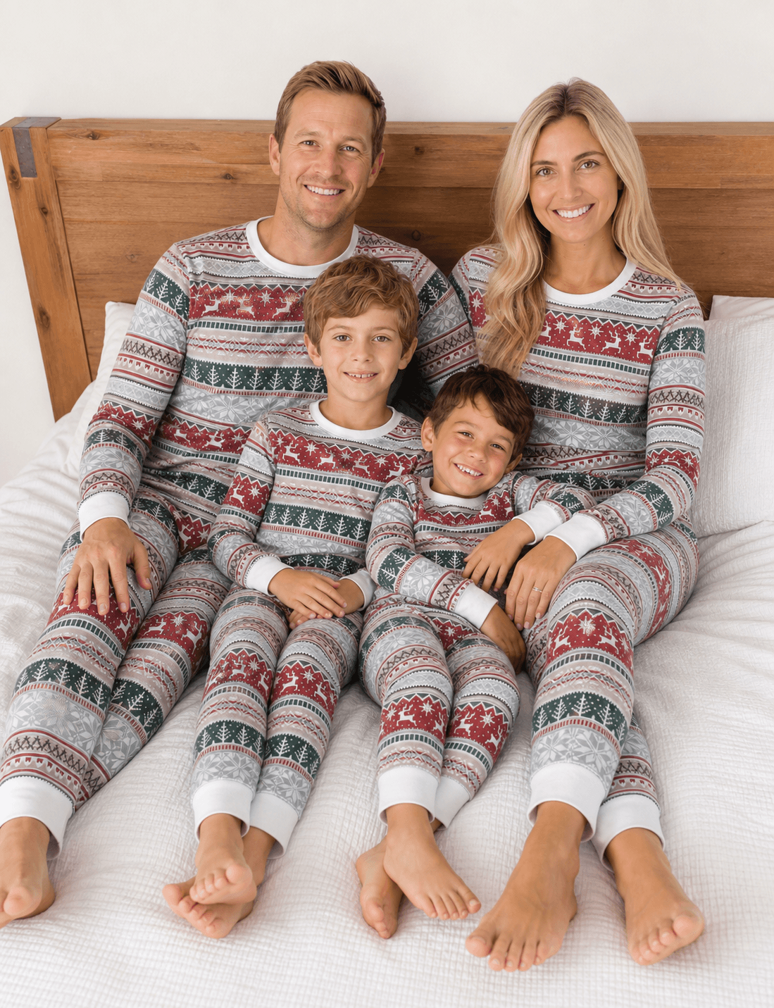 Genitori e due bambini in posa su un letto, in pigiami natalizi Fair Isle coordinati rossi, verdi e bianchi.
