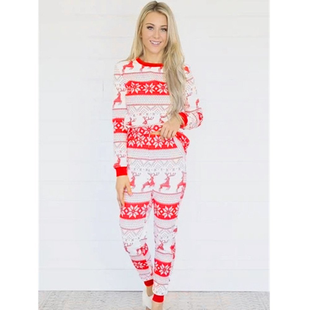 Woman modeling red-and-white reindeer and snowflake Christmas pajamas with red cuffs against a white wall.
