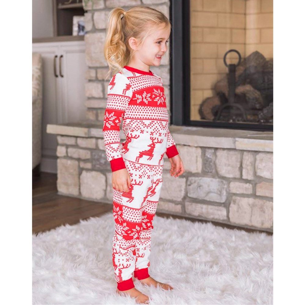 Side view of a girl beside a fireplace in red-and-white reindeer and snowflake Christmas pajamas with red cuffs.