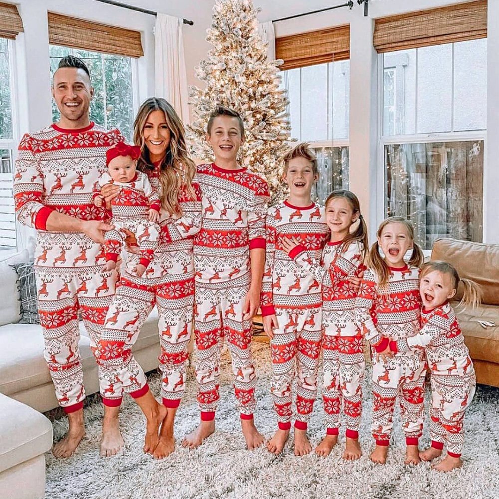 Parents and six children posing beside a Christmas tree in matching red-and-white reindeer and snowflake pajamas.
