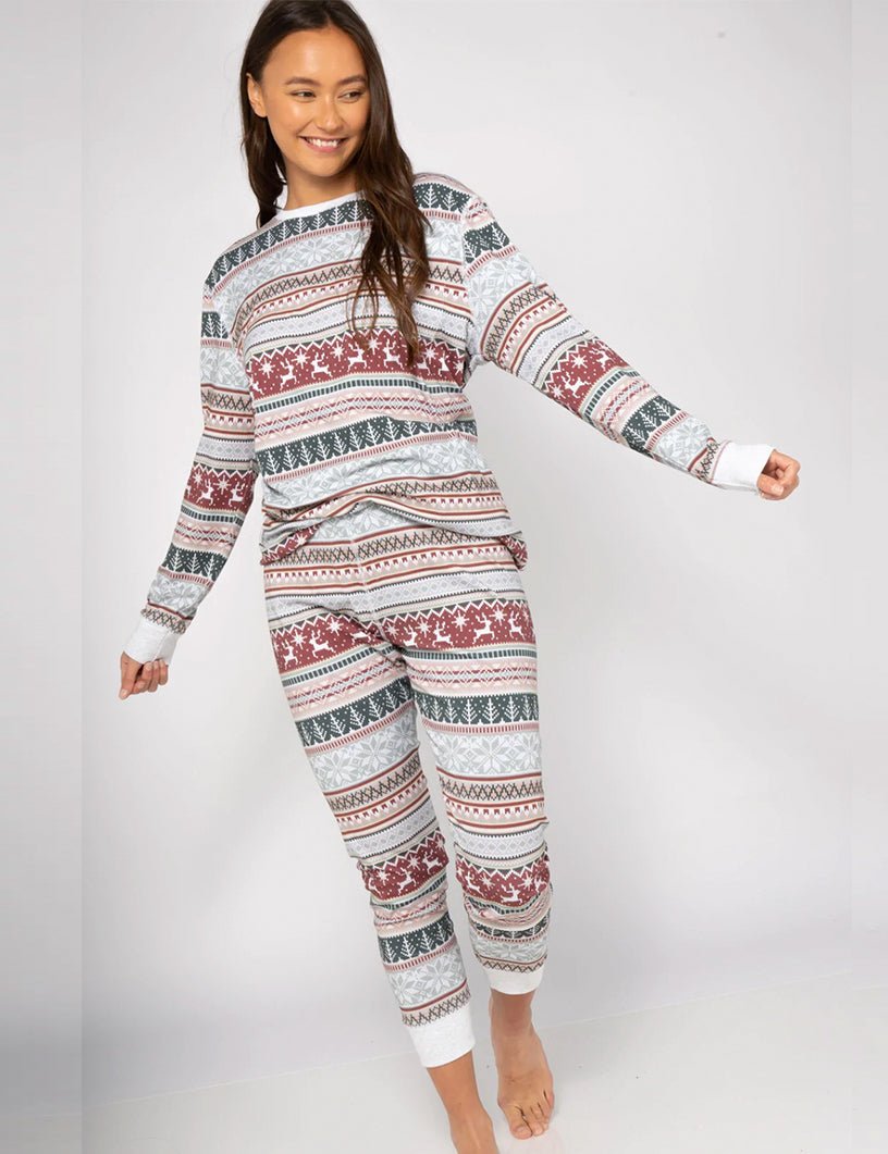 Woman in Fair Isle Christmas Pajamas Smiling – White Base with Red Reindeer Green Tree and Blue Snowflake Stripe Print, Relaxed Fit Long Sleeve Set