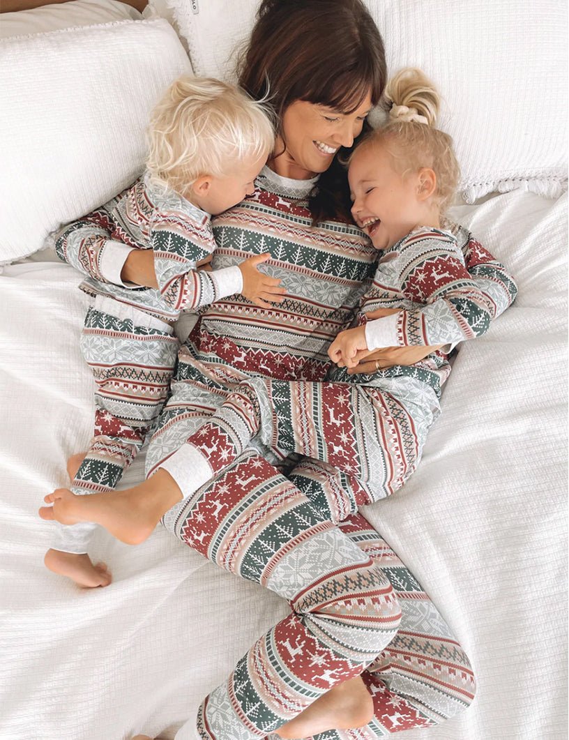 Mom Lying on White Bed Cuddling Two Laughing Toddlers in Matching Fair Isle Christmas Pajamas – Overhead View of Cozy Holiday Morning