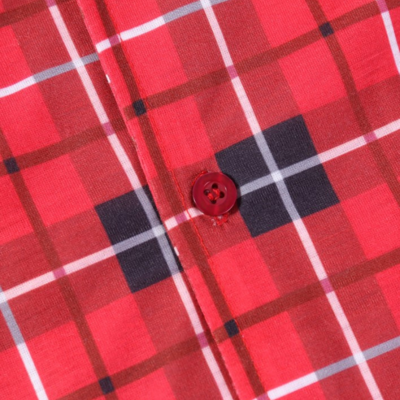 Nahaufnahme eines roten Knopfes und der genähten vorderen Knopfleiste an einem rot-schwarz-weißen Tartan-Weihnachtspyjamaoberteil.