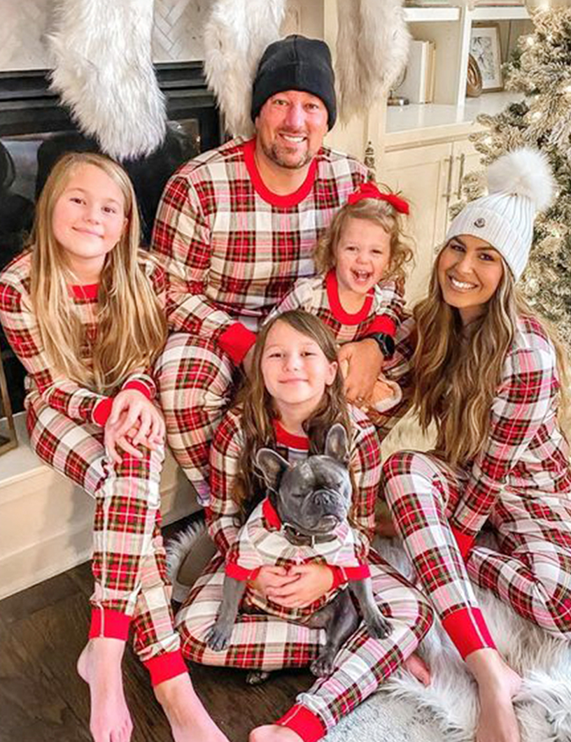 Familie mit einem Hund sitzt an einem Kamin in creme-rot-grün karierten Weihnachtspyjamas mit roten Bündchen.