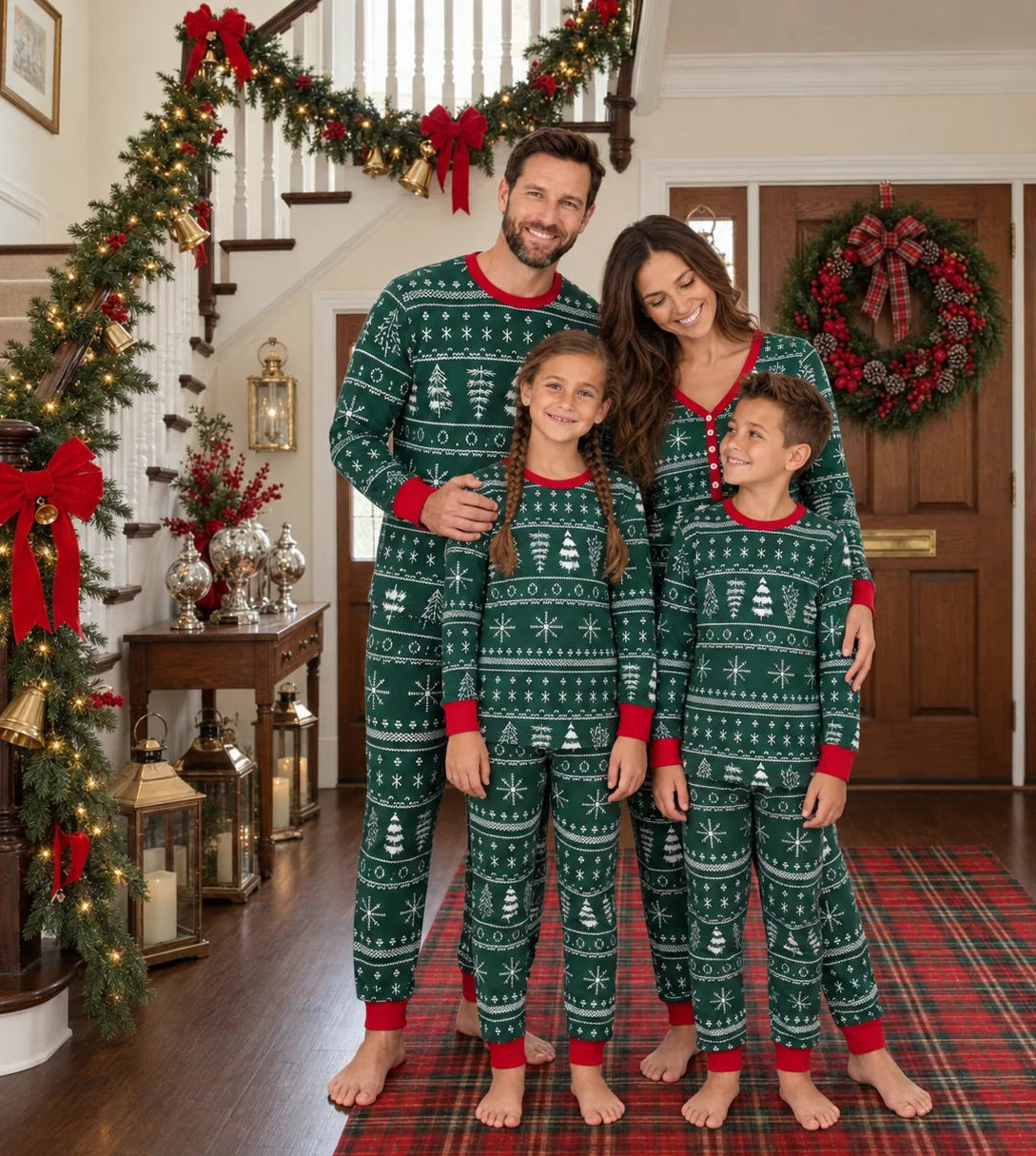 Family standing in dark green Fair Isle Christmas pajamas on a plaid runner beside a garland-covered staircase.
