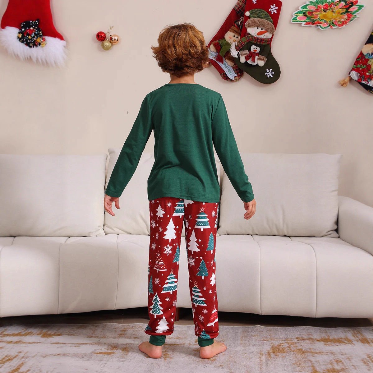 Vista posteriore di un bambino con maglia verde del pigiama in tinta unita e pantaloni rossi con alberi di Natale, fiocchi di neve e bordi verdi.