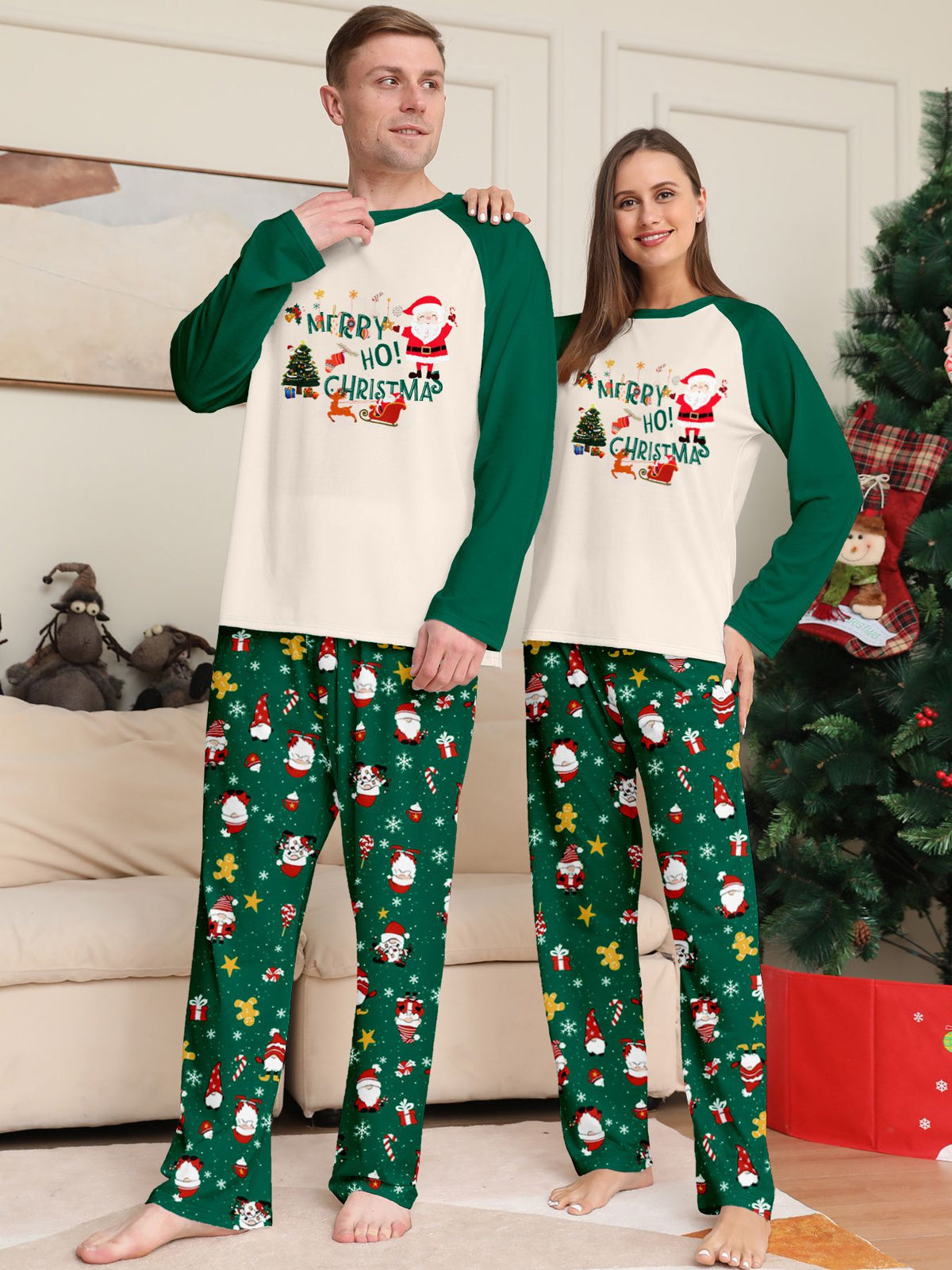 Coppia accanto a un albero con maglie color crema con motivo natalizio e maniche raglan verdi e pantaloni verdi del pigiama con Babbo Natale.