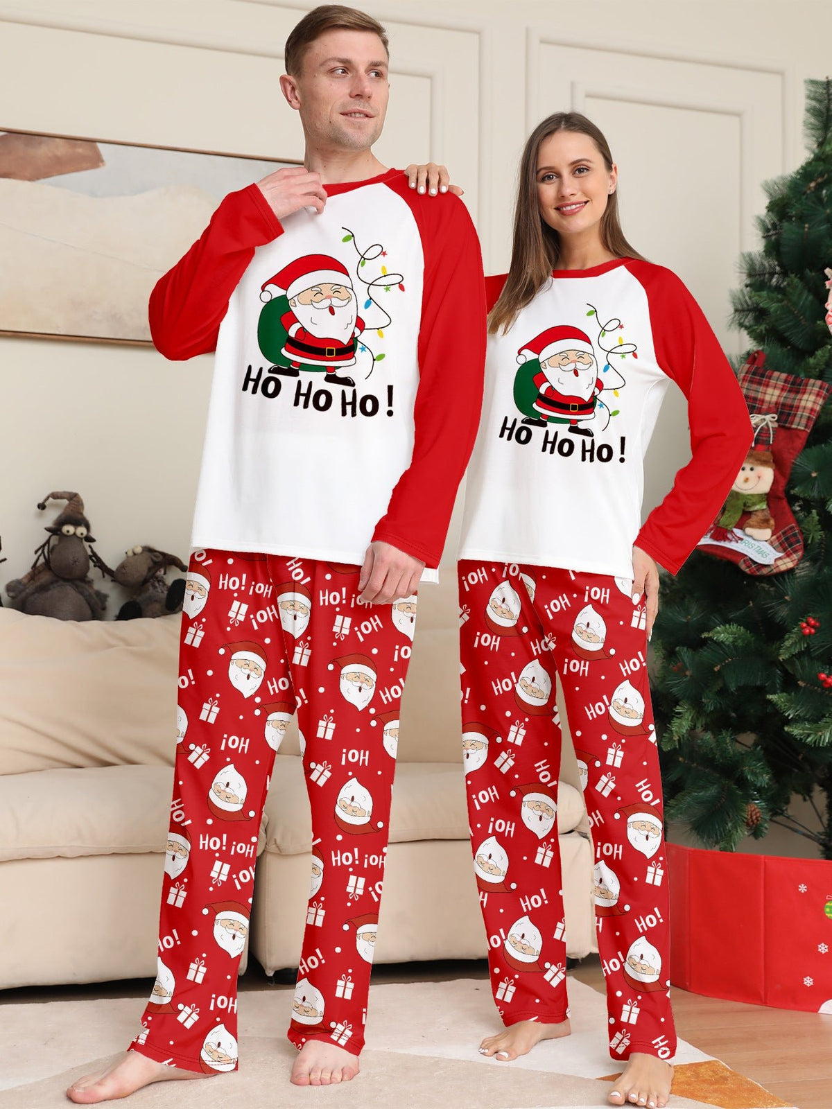 Couple beside a tree in matching white Santa pajama tops with red raglan sleeves and red Santa print pants.