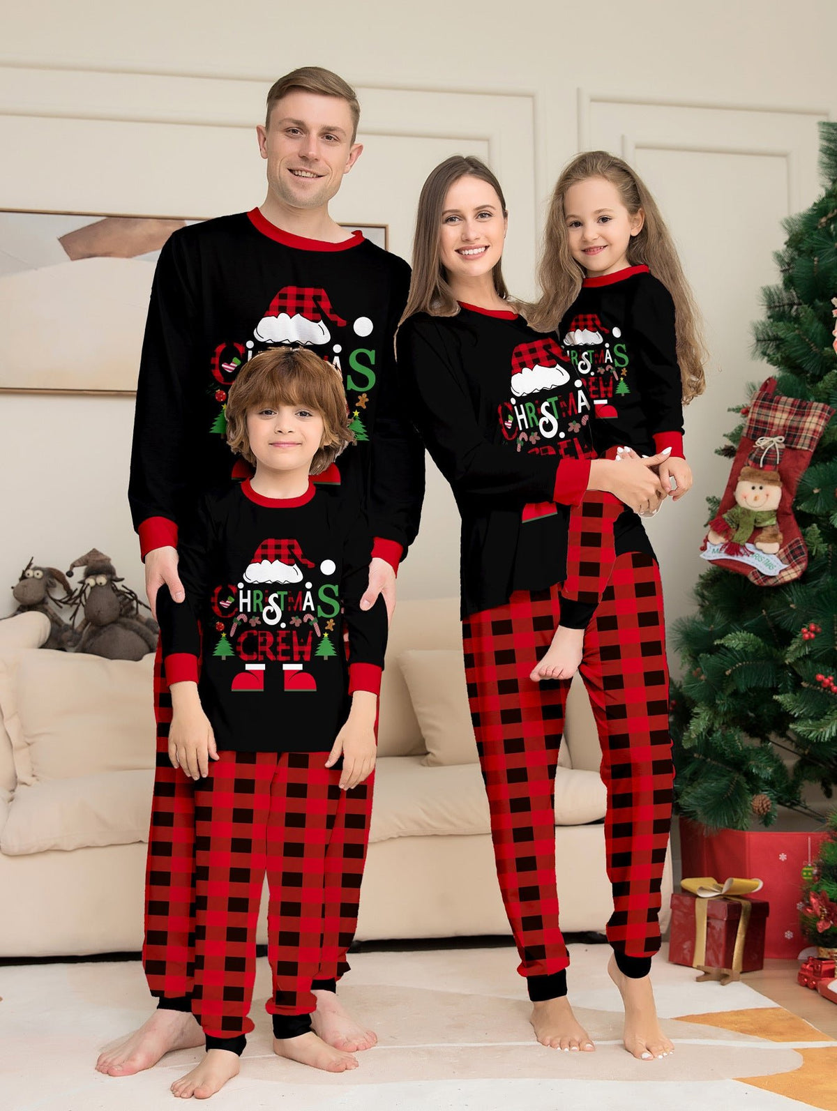 Famiglia accanto a un albero con maglie nere Christmas Crew del pigiama con bordi rossi e pantaloni a grandi quadri rossi e neri.