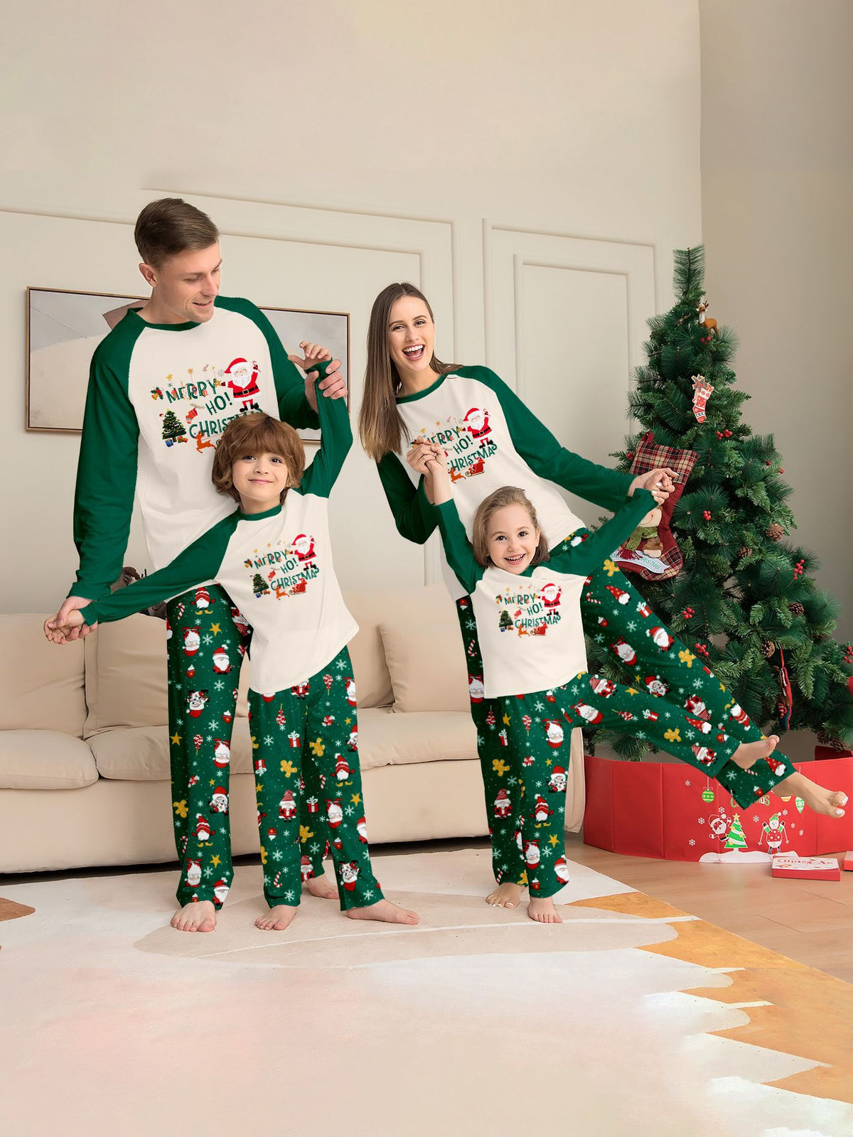 Famiglia che gioca accanto a un albero con maglie color crema con motivo natalizio e maniche verdi e pantaloni verdi del pigiama con Babbo Natale.