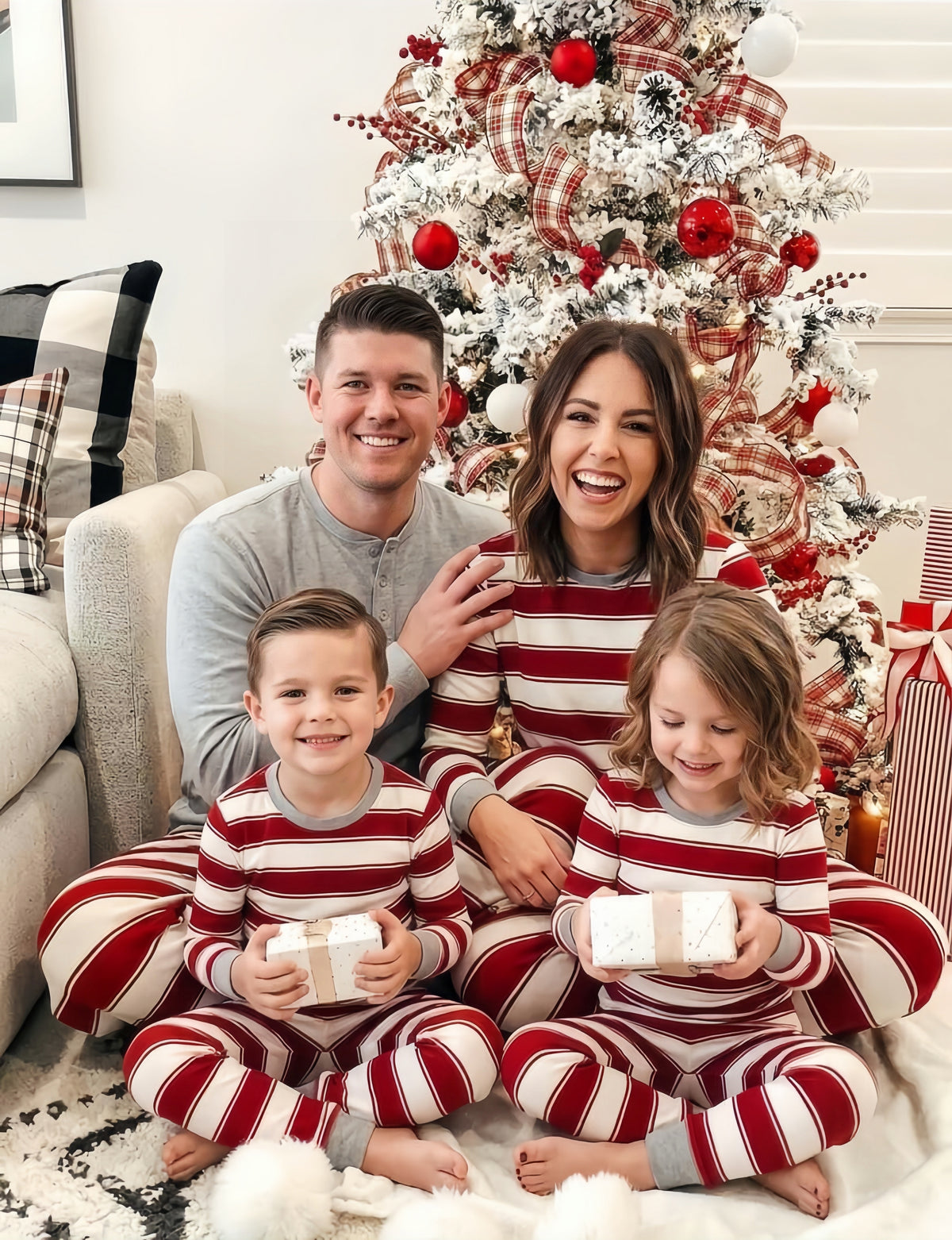 Happy family holding holiday gift boxes by Christmas tree in matching striped pajamas