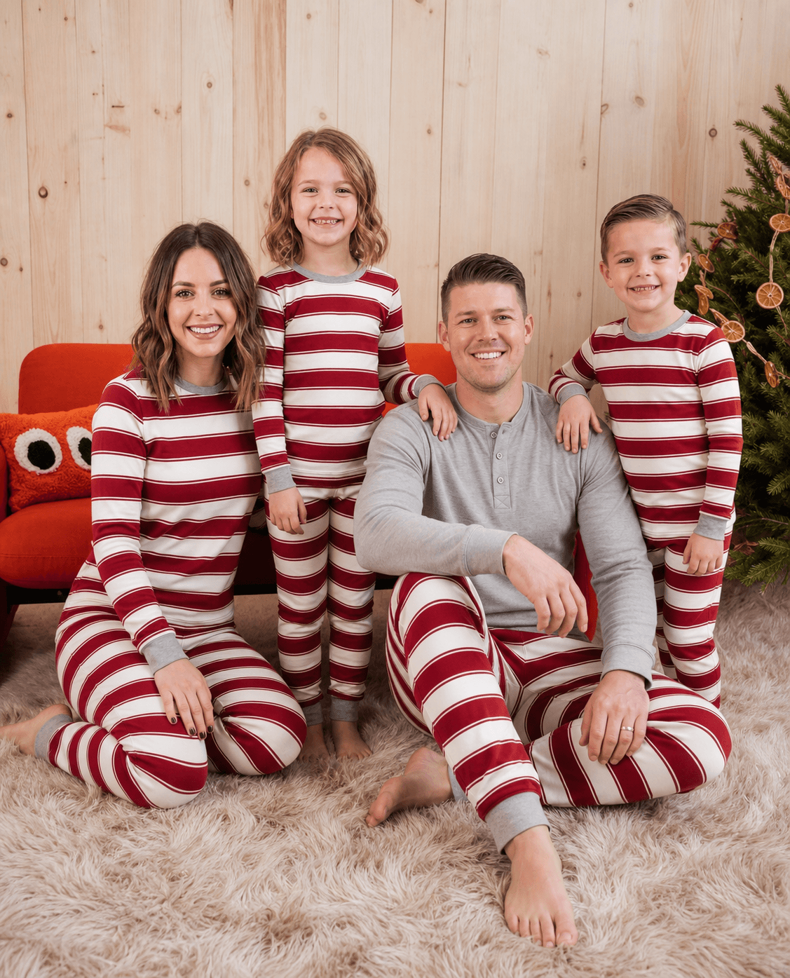 Cozy family sitting together on white rug in red and white stripe matching holiday sleepwear