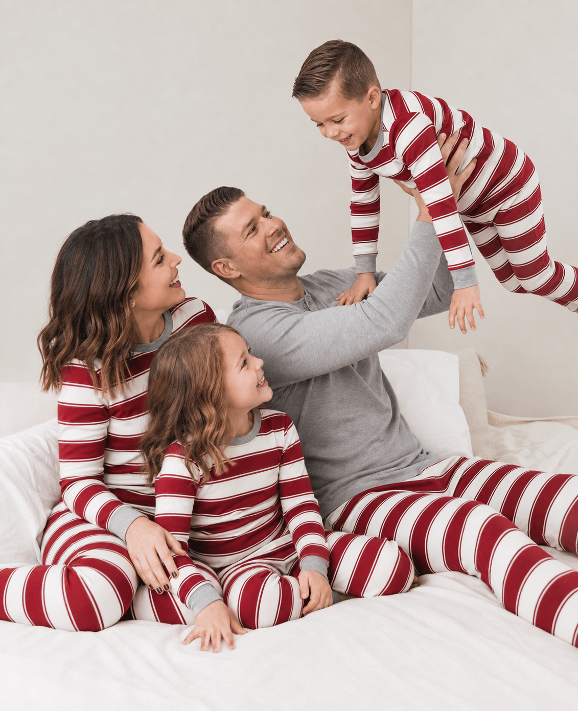 Parents, kids, and dog relaxing on bed in matching red and white striped Christmas pajamas