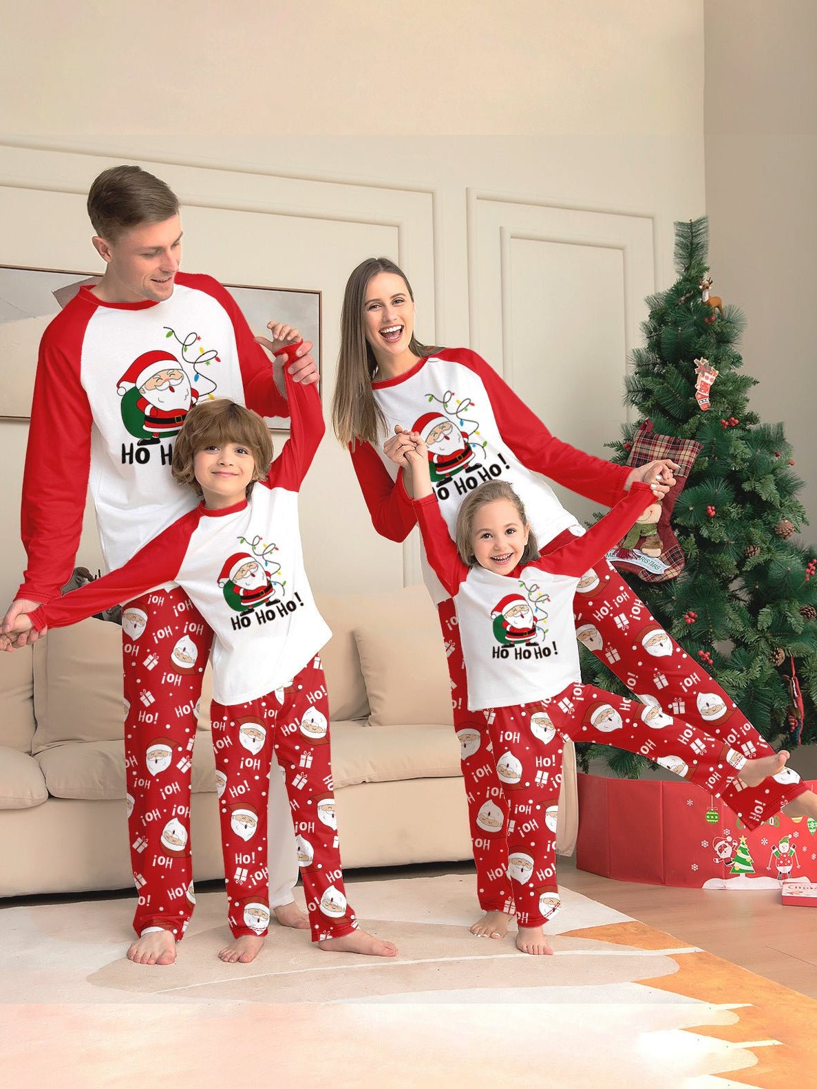 Family playing beside a Christmas tree in white Santa graphic tops with red sleeves and red Santa print pajama pants.