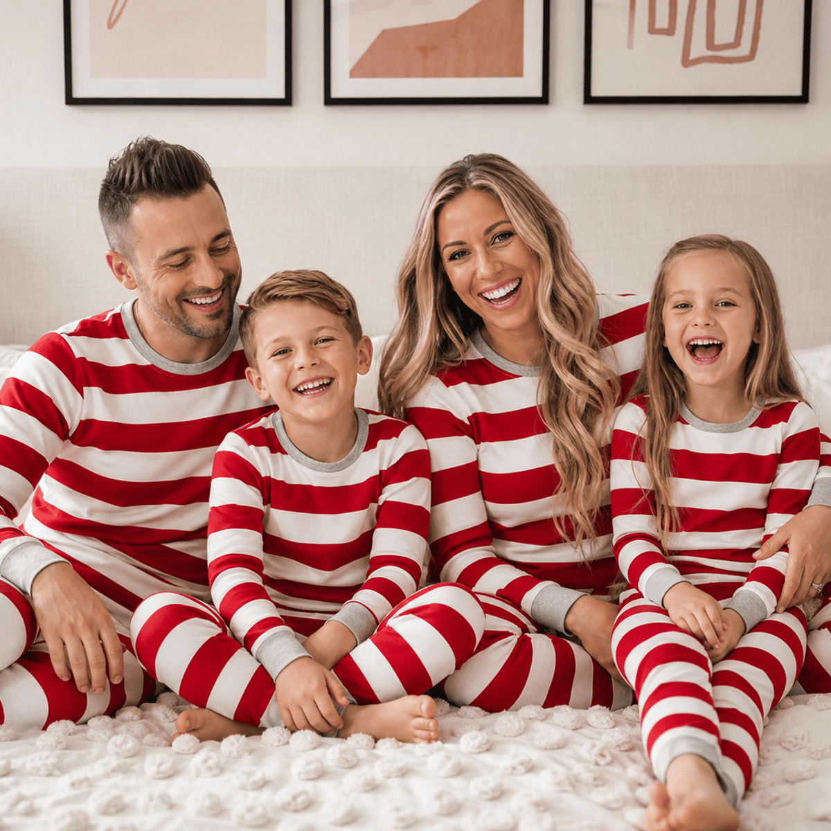 Genitori e due bambini seduti su un letto, in pigiami natalizi coordinati a righe rosse e bianche con polsini grigi.