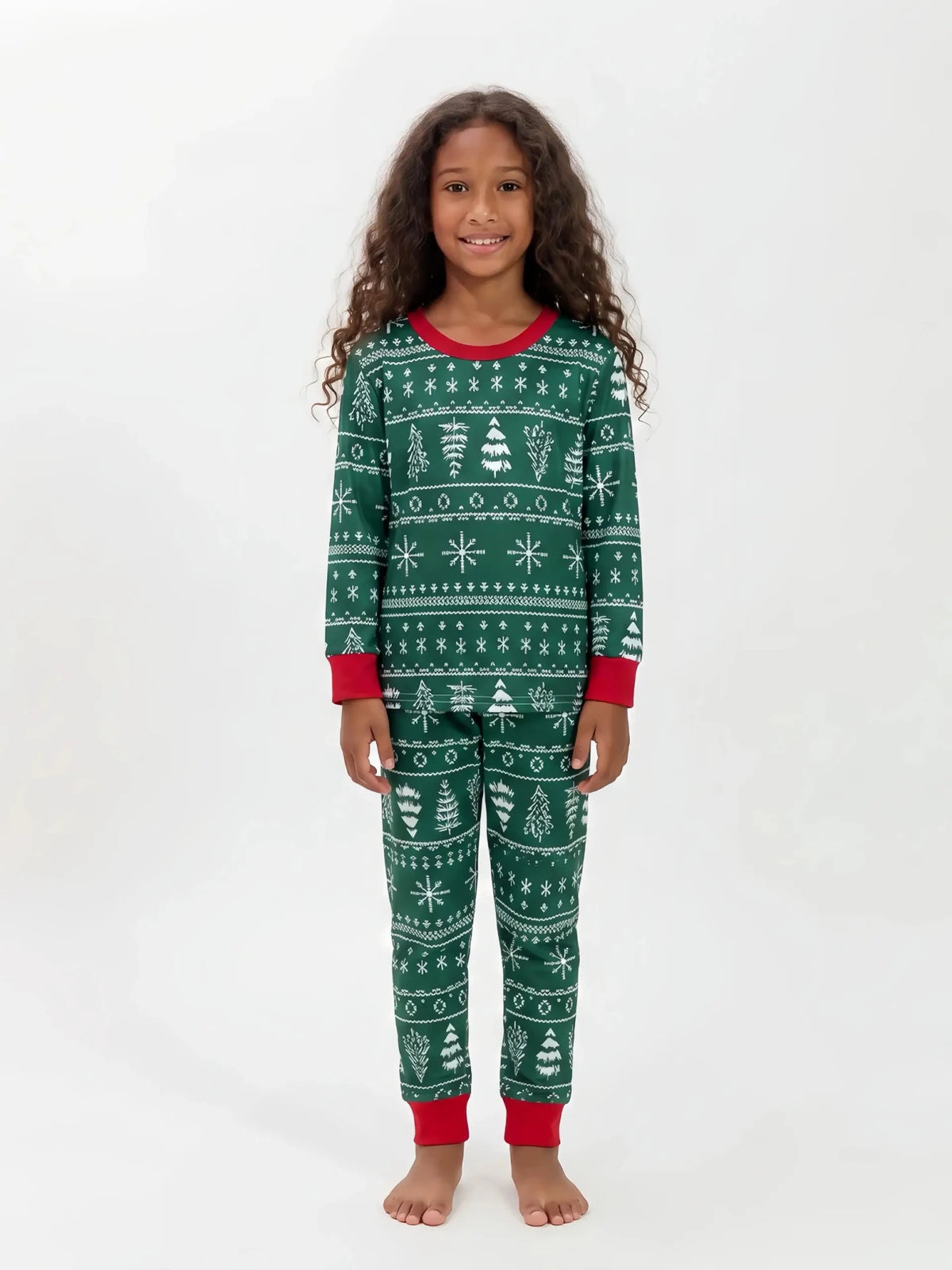 Bambina che presenta un pigiama natalizio verde con fasce di alberi e fiocchi di neve bianchi e bordi rossi, su sfondo bianco.