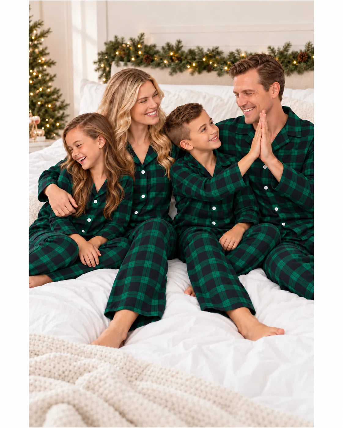 Father and son high-five as the family sits on a bed in matching green and black plaid pajamas.