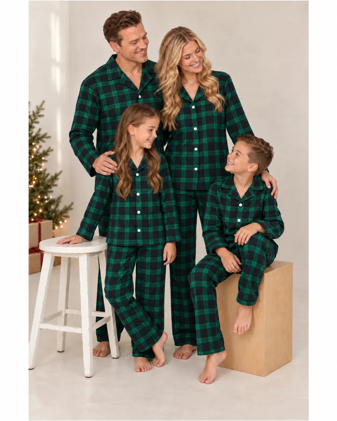 Parents and children model green and black plaid pajamas beside a stool and wooden cube.