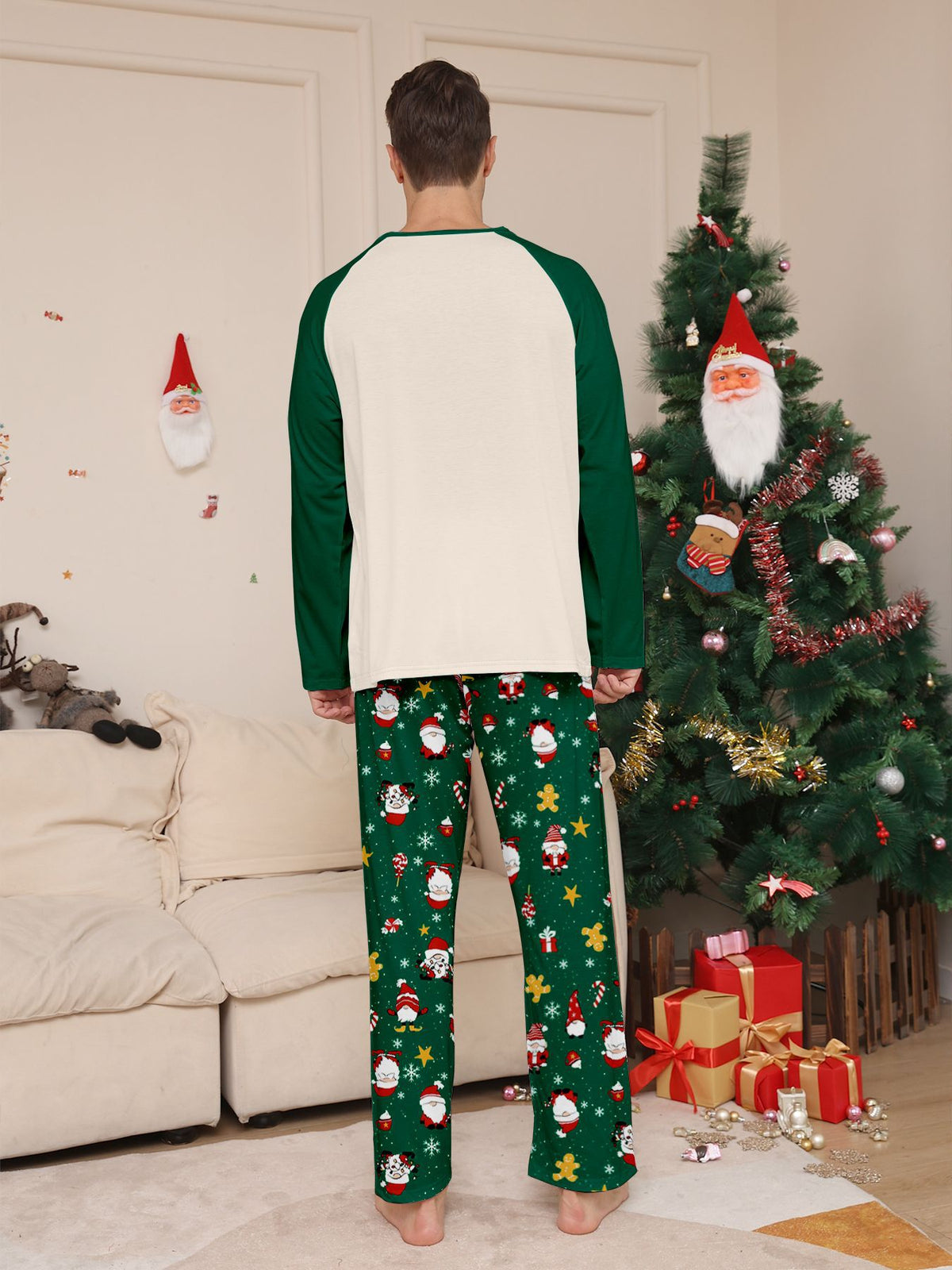 Vista posteriore di un uomo con maglia color crema del pigiama in tinta unita e maniche raglan verdi e pantaloni verdi con Babbo Natale, accanto a un albero.