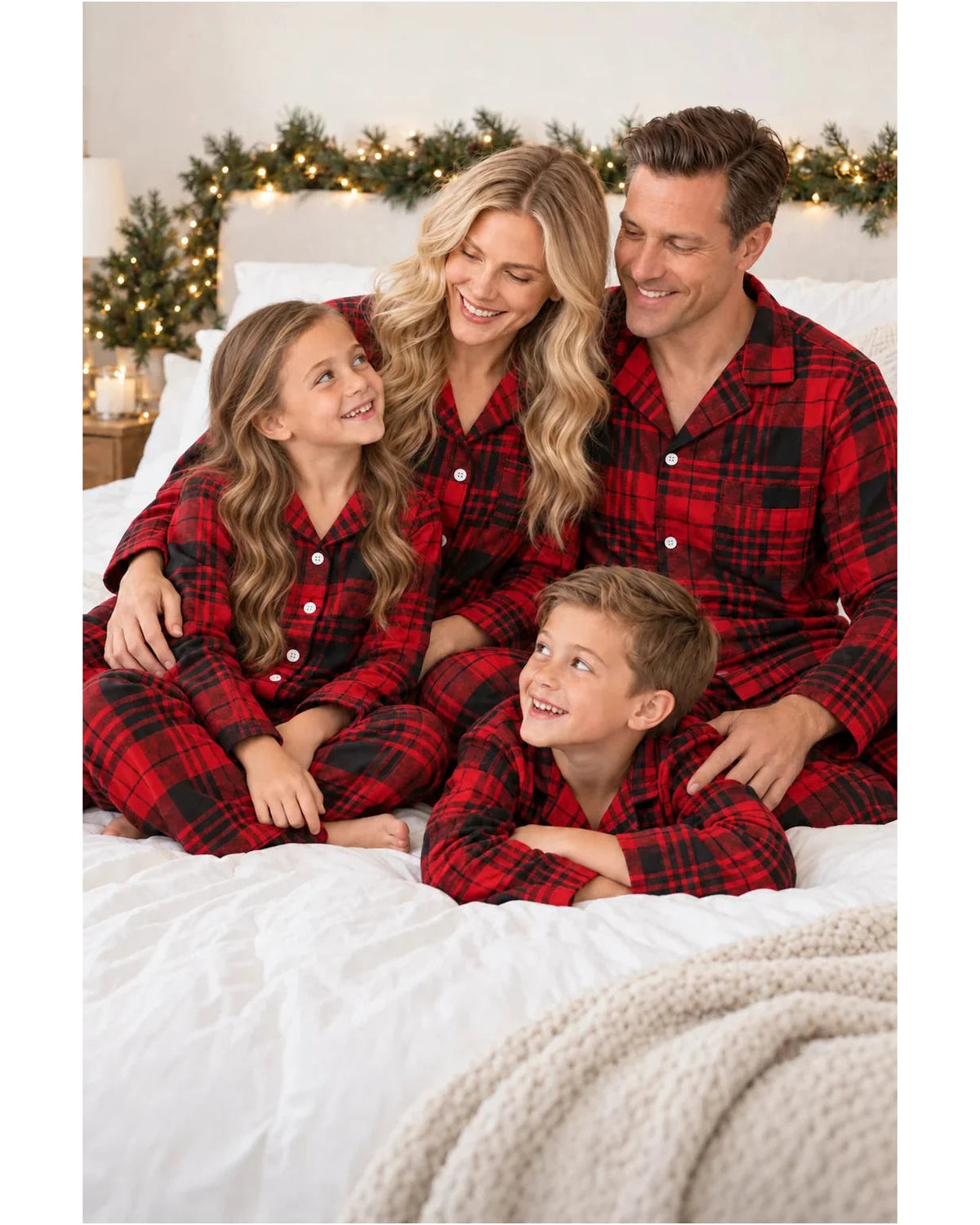 Parents and children cuddling on a white bed in matching red and black tartan pajamas.