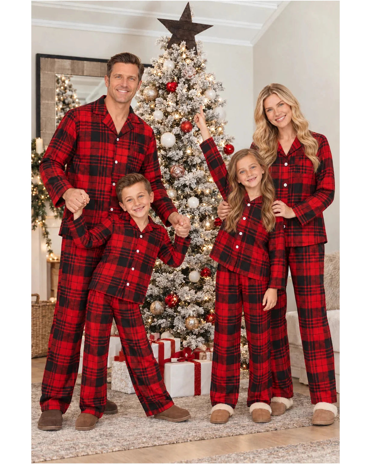 Family wearing red and black tartan pajama sets and raising their arms beside a Christmas tree.