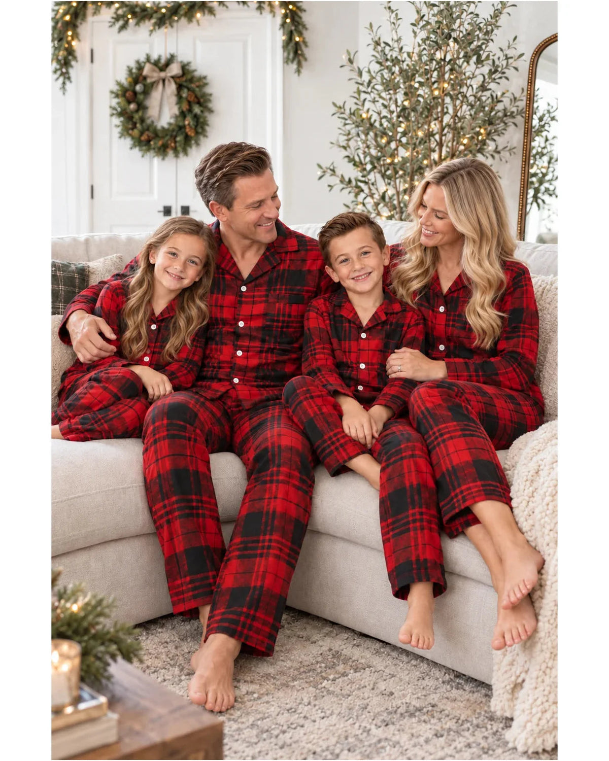 Family of four sitting together on a sofa in matching red and black tartan pajamas.