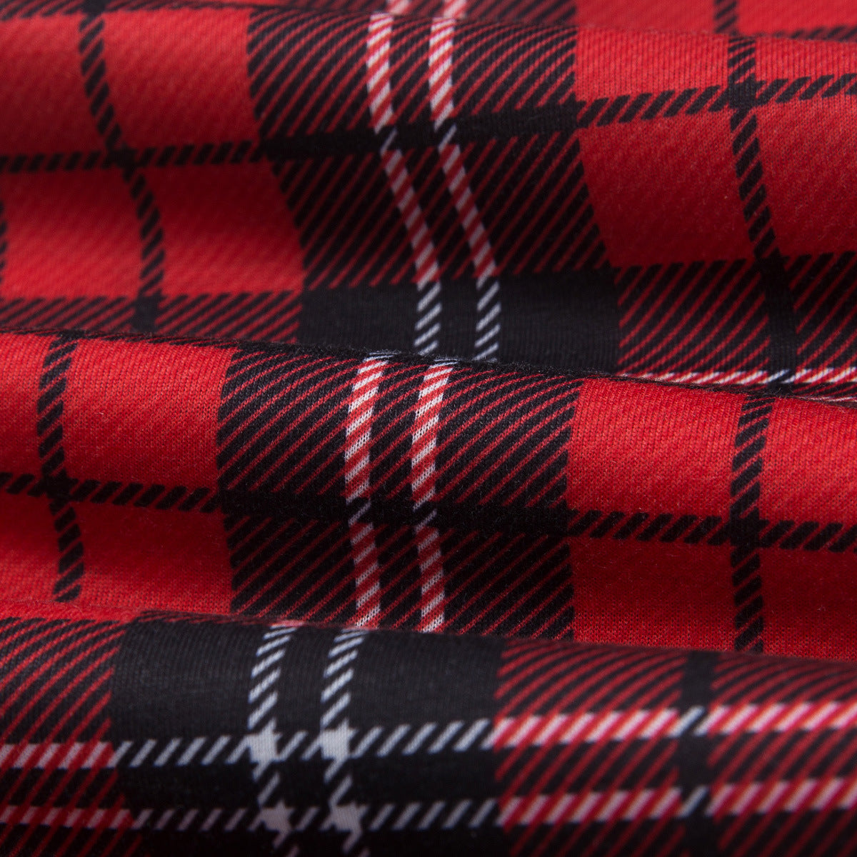 Primo piano di tessuto piegato del pigiama in tartan rosso, nero e bianco, con motivo a quadri e trama della superficie.