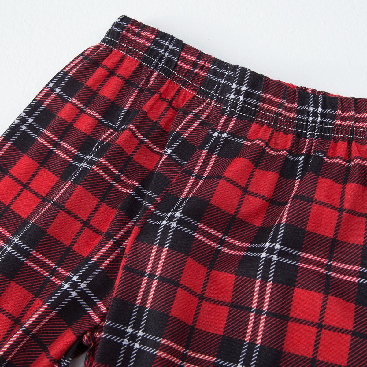 Primo piano della vita elasticizzata e delle cuciture dei pantaloni del pigiama natalizio in tartan rosso, nero e bianco.