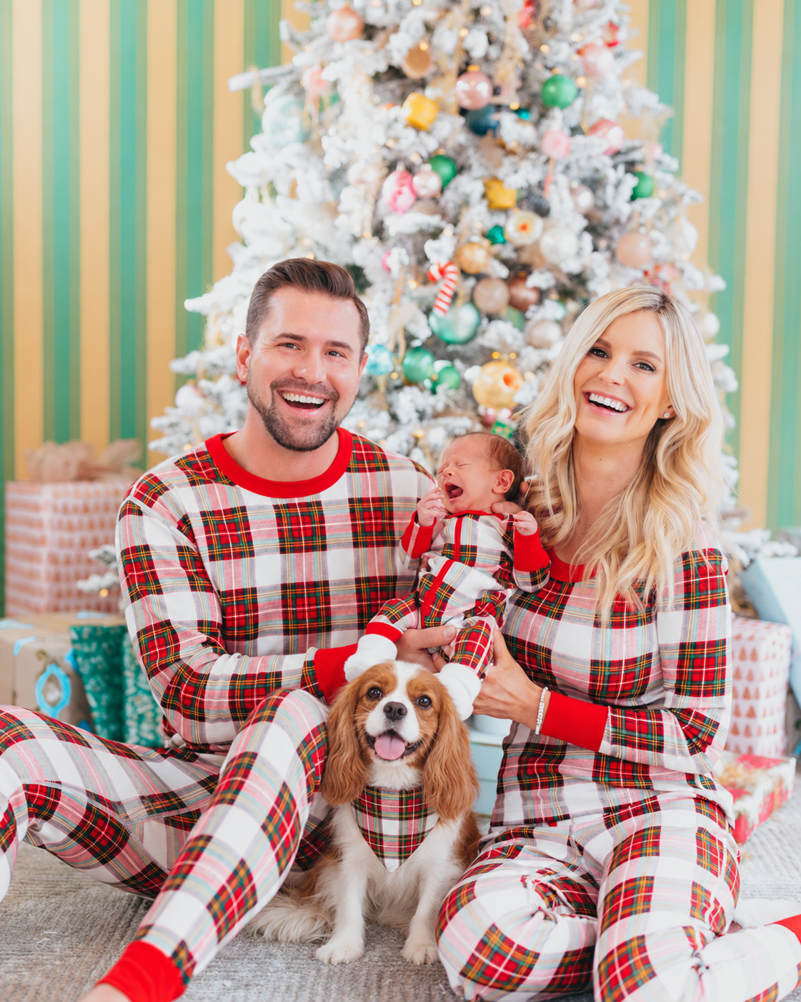 Family in tartan Christmas pajamas with a chestnut and white Cavalier King Charles Spaniel wearing a matching triangular tartan bandana.