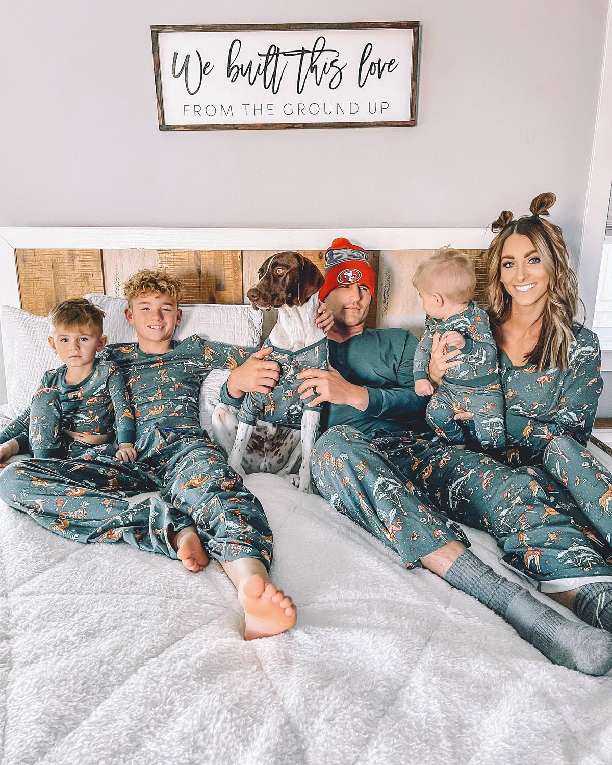 Familie entspannt auf einem Bett neben einem Hund in petrolfarbenen Weihnachtspyjamas mit Tiermuster.