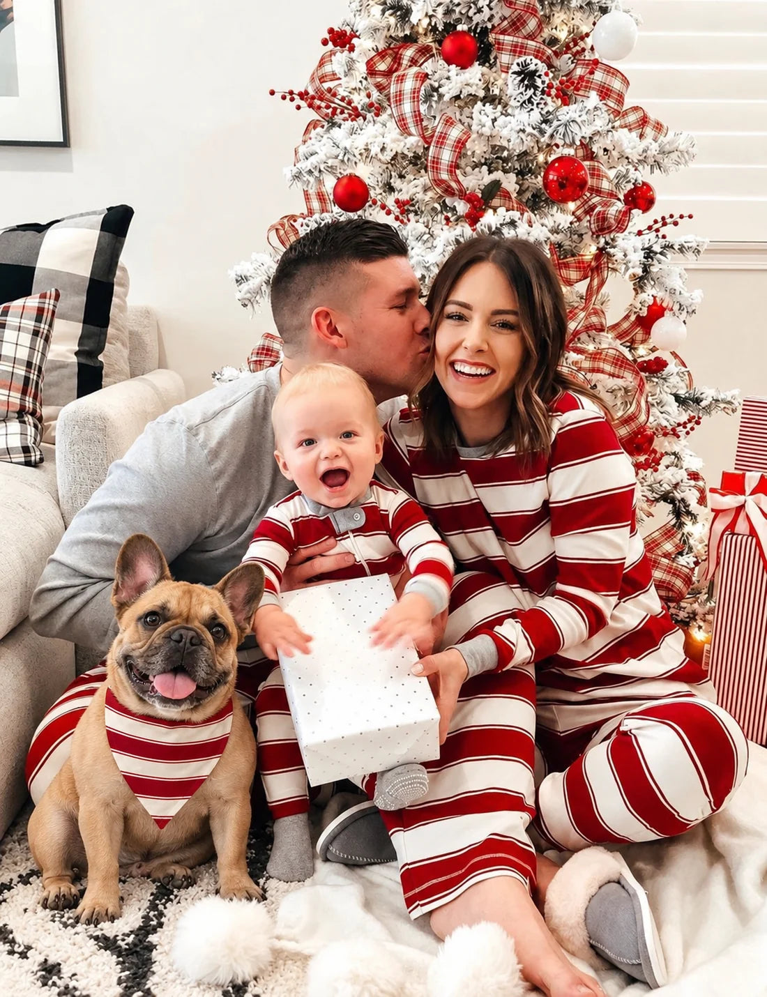 Parents and baby in red and white striped pajamas with a gray top on the man, and a dog in a striped bandana.