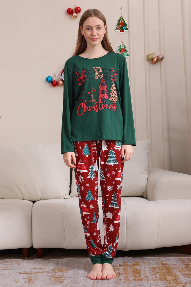 Donna che presenta una maglia verde Merry Christmas del pigiama e pantaloni rossi con alberi e fiocchi di neve e bordi verdi, accanto a un divano.