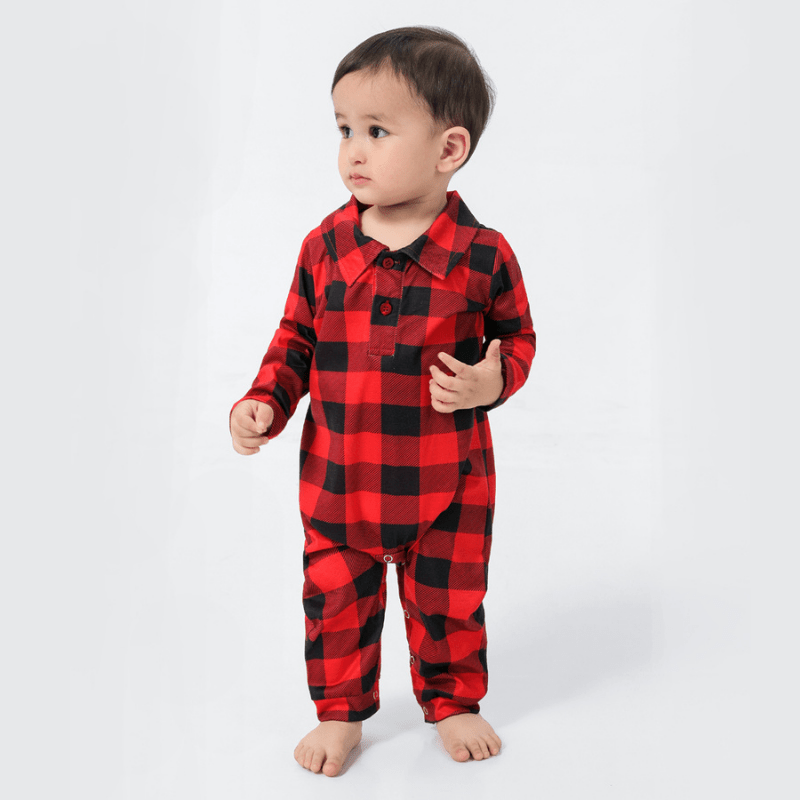 Toddler wearing a red and black buffalo plaid collared one-piece sleeper against a white background.