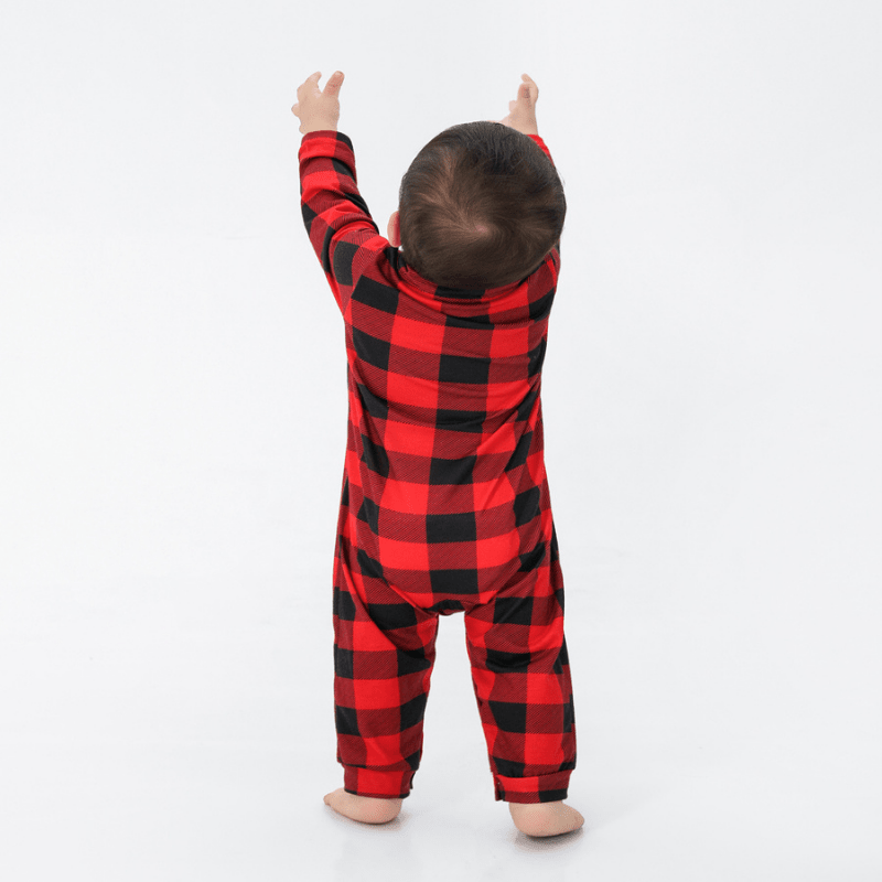 Rear view of a toddler in a red and black buffalo plaid one-piece sleeper with both arms raised.