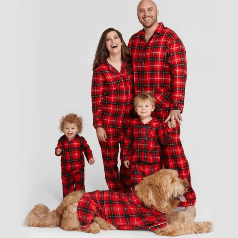 Famiglia e cane in posa con pigiami natalizi in tartan rosso, con maglie con colletto abbottonate davanti, su sfondo bianco.